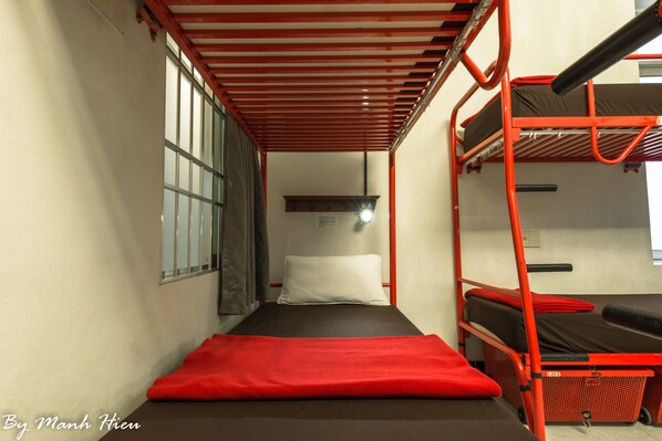 Habitación estrecha con literas, un tapete rojo en el suelo y una ventana con barrotes.