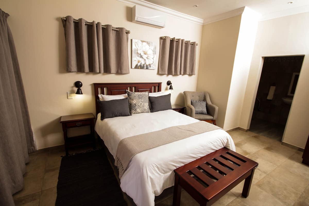 A hotel room with a large bed, two bedside tables, a chair, and a wooden bench.