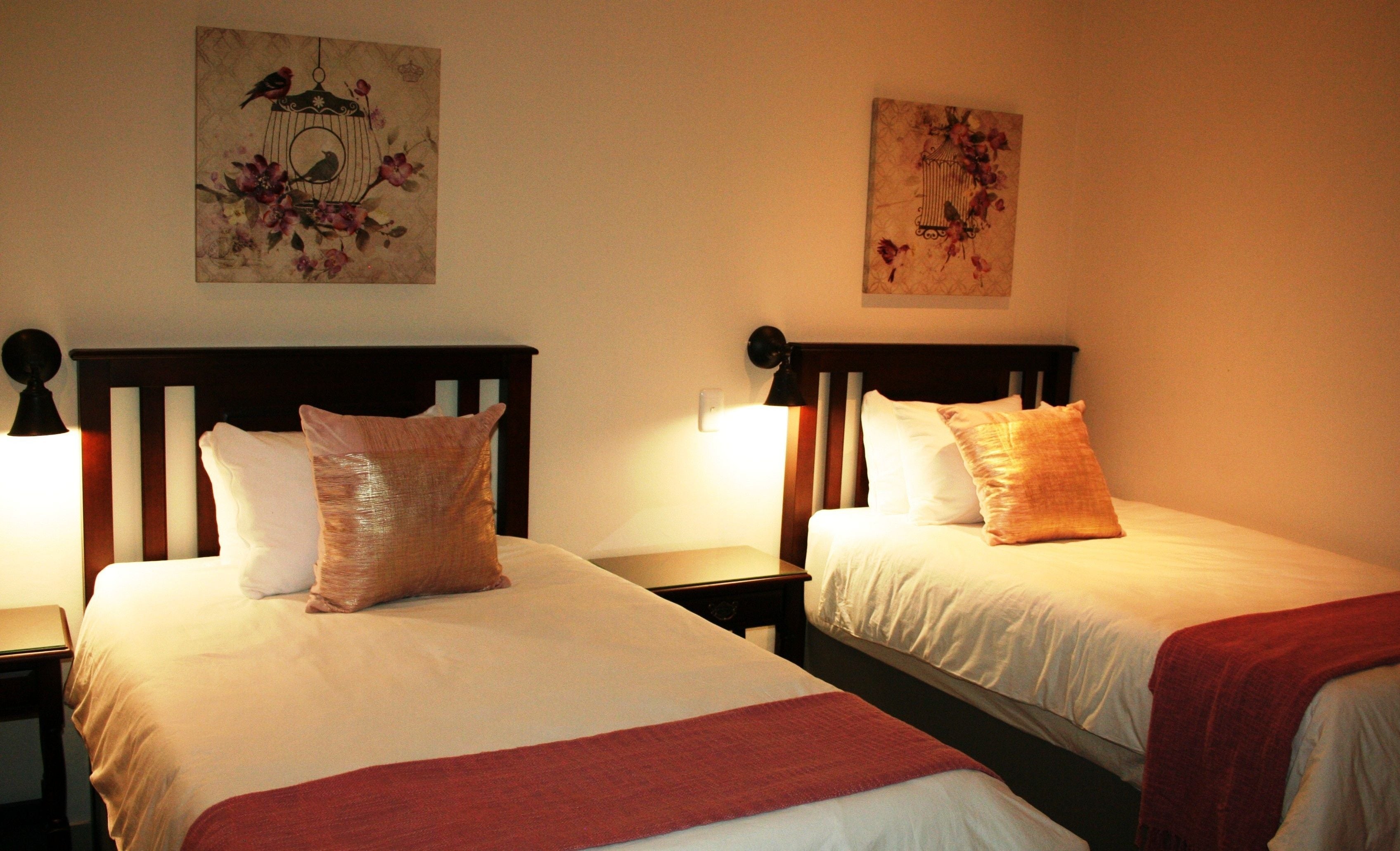 Two single beds with wooden headboards, white linens, and red throw blankets.