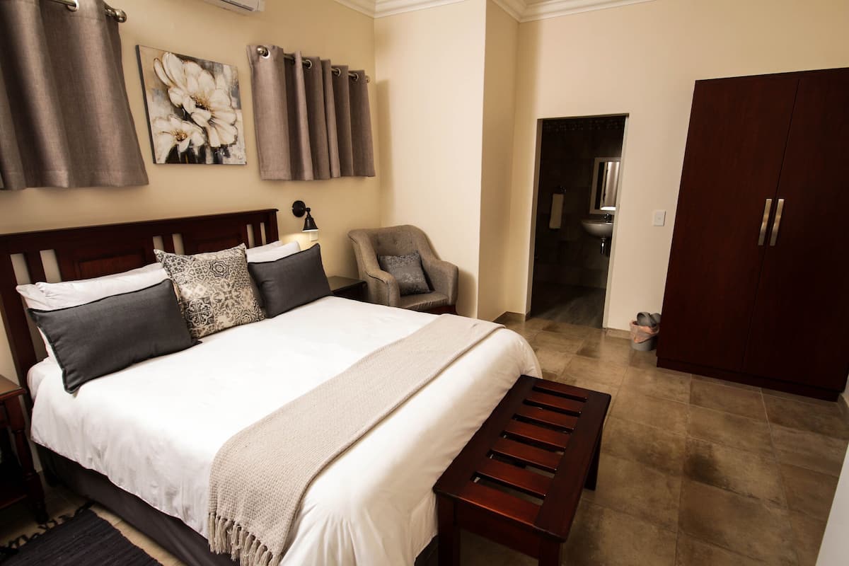 A bedroom with a large bed, a chair, a wardrobe, and a bathroom visible through an open door.