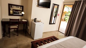 Ein Hotelzimmer mit einem Bett, einem Schreibtisch mit Stuhl, einem kleinen Kühlschrank, einem an der Wand befestigten Fernseher und einer Glastür zu einem Außenbereich.