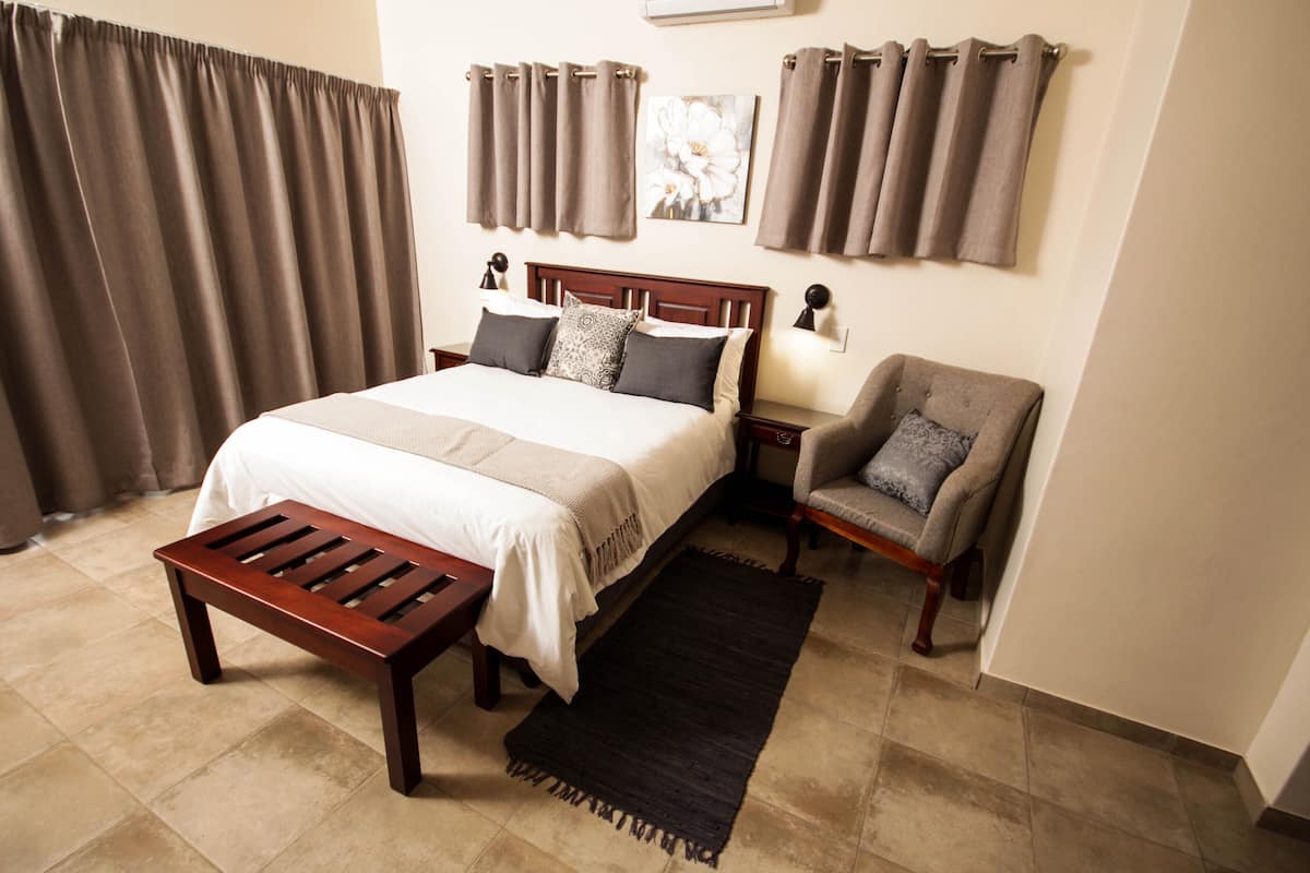 A neatly arranged bedroom with a bed, bedside table, chair, and a small wooden bench.