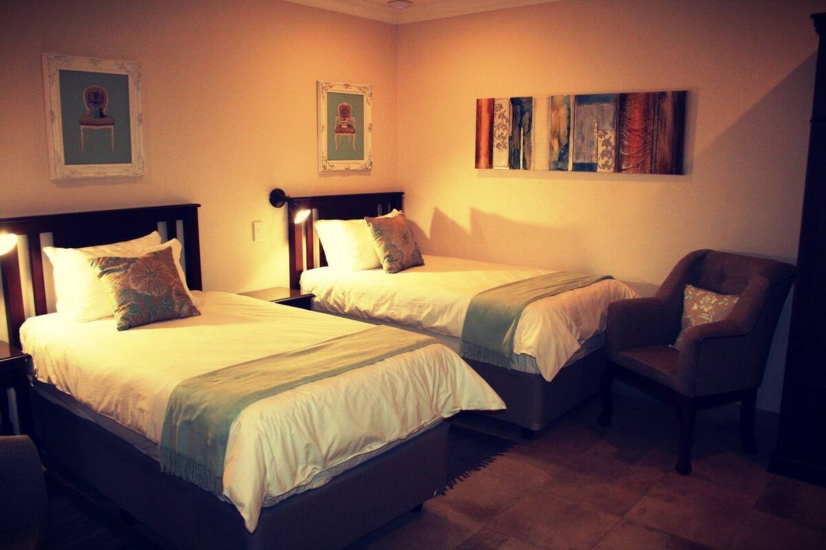 A hotel room with two single beds, a chair, and artwork on the walls.