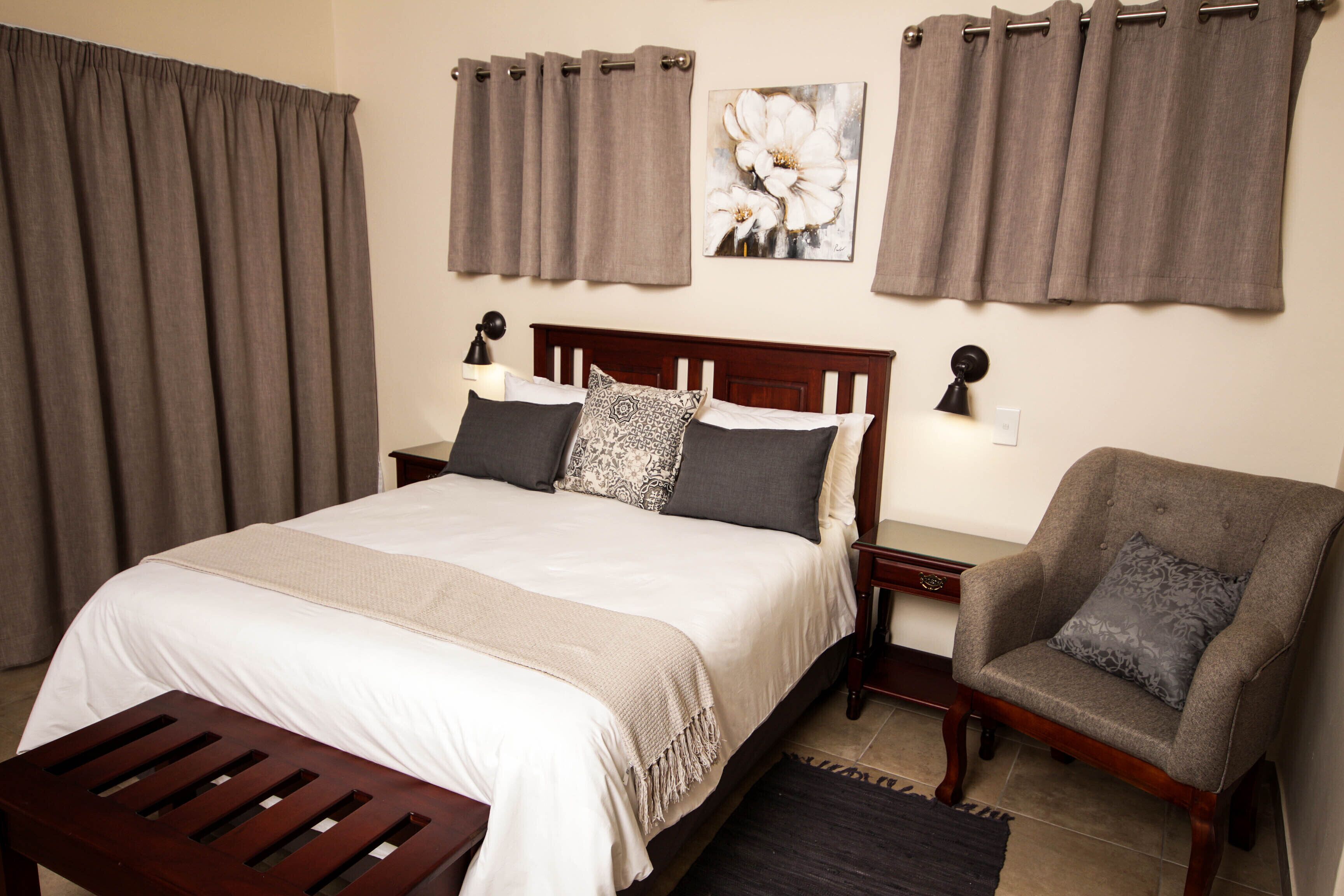 A neatly arranged bedroom with a large bed, a bedside table with a lamp, a chair, and a rug.