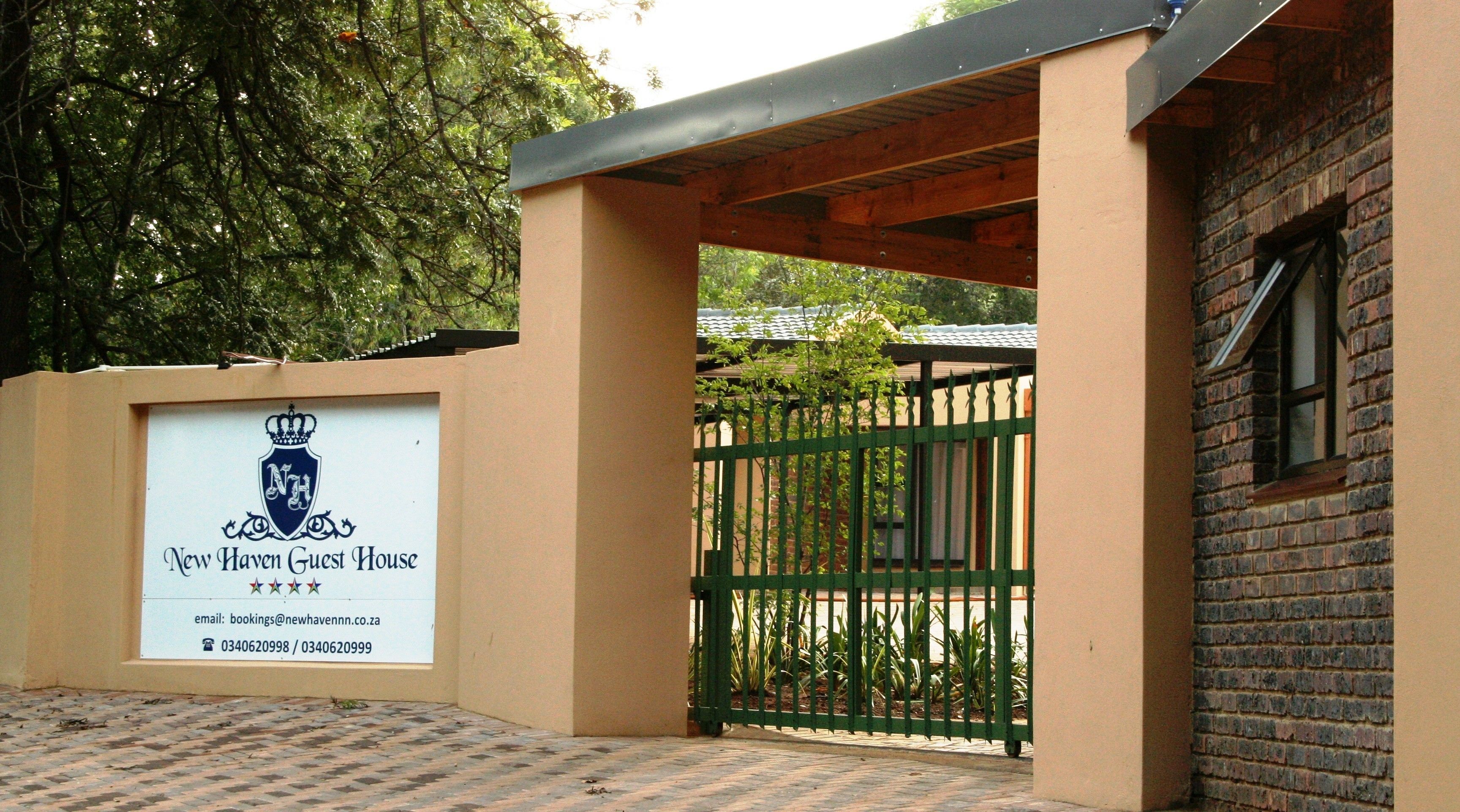 A gated entrance to a property with a signboard displaying the name "New Haven Guest House" and contact information.