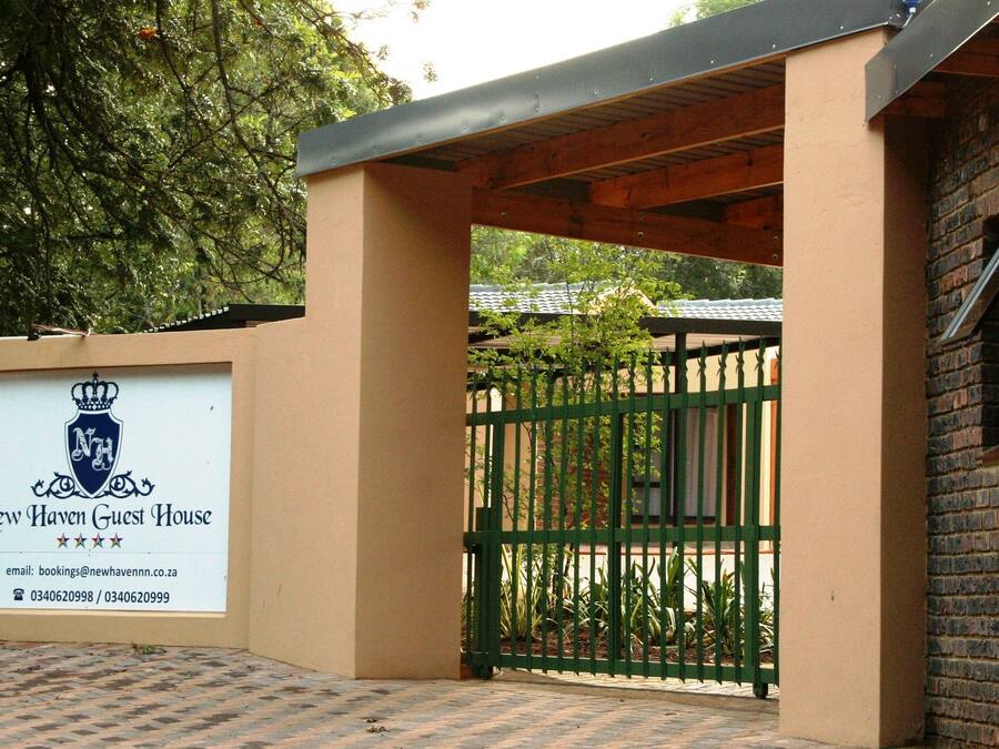 A gated entrance to a property with a signboard displaying the name "New Haven Guest House" and contact information.