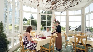 A conservatory with a dining table set for four, surrounded by wooden chairs. - Hotel Zum Baeren (Altenberg)