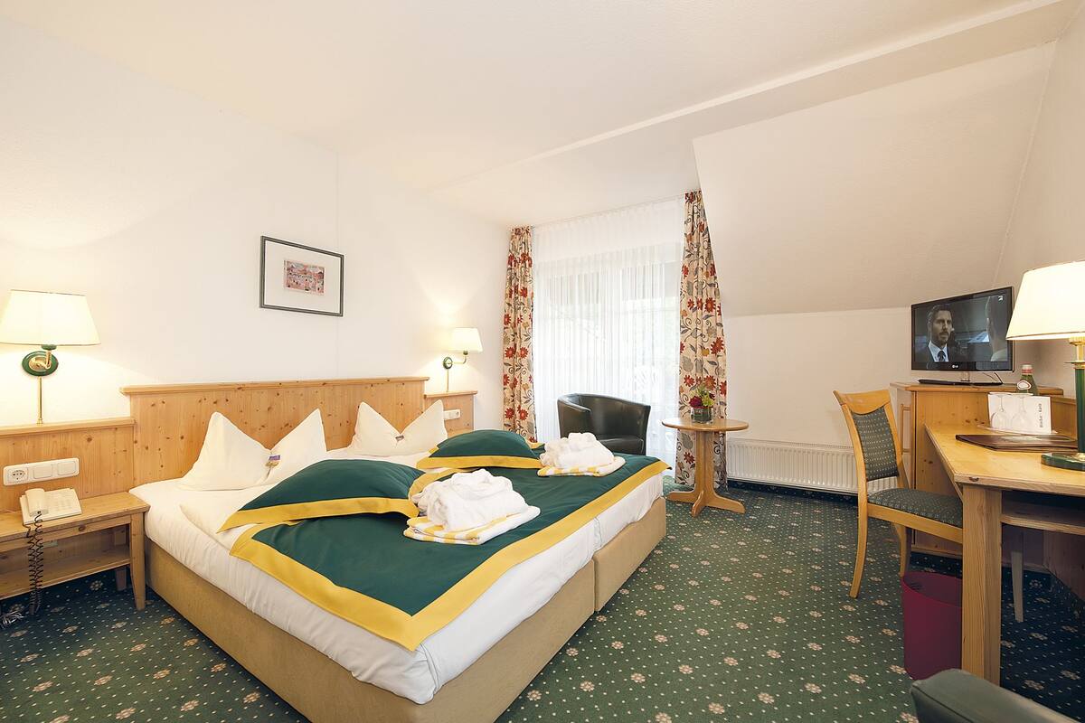 Une chambre d’hôtel comprenant un lit, deux tables de chevet, un bureau, une chaise, un téléviseur et une fenêtre avec des rideaux.