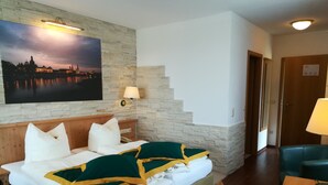 A hotel room with a bed, a nightstand, a lamp, a painting of a cityscape, and a staircase. - Hotel Zum Baeren (Altenberg)