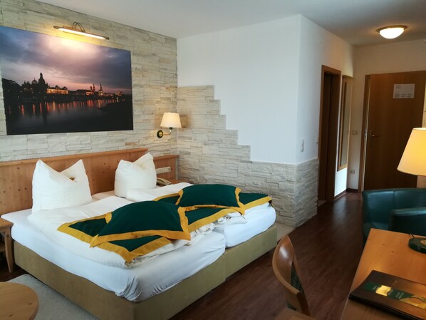 Habitación de hotel con una cama, una mesita de noche, una lámpara, un cuadro de un paisaje urbano y una escalera.