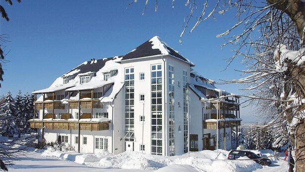 A multi-story hotel with balconies, surrounded by snow-covered trees and a clear sky. - Hotel Zum Baeren (Altenberg)