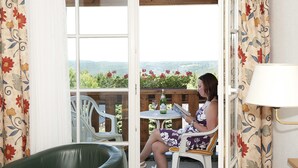 A woman sitting at a table by a window with a view of greenery and hills. - Hotel Zum Baeren (Altenberg)