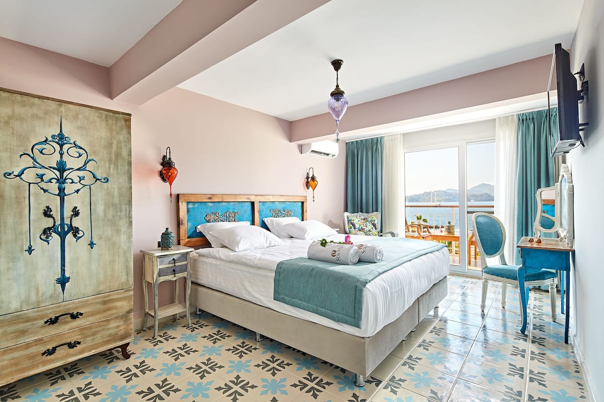 Un dormitorio con cama, mesita de noche, cómoda, escritorio con silla y un ventanal con vistas.