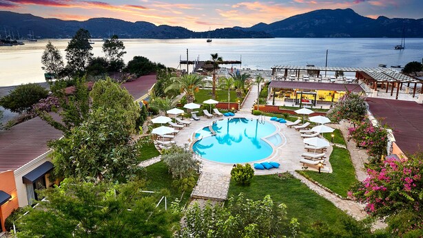 A resort with a central swimming pool, lounge areas, and a view of the lake and mountains.