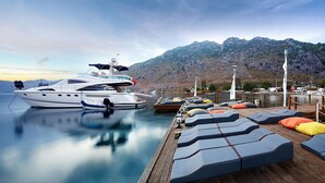 A yacht docked at a marina with a wooden deck and lounge chairs.