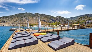 A wooden pier with lounge chairs and a flag labeled "Solito" extending into a body of water, with mountains in the background.