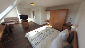 Una habitación amplia con una cama grande, televisión, sofá y armario de madera.