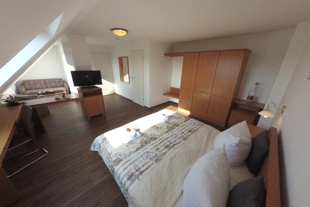 A spacious room with a large bed, a TV, a sofa, and a wooden wardrobe.