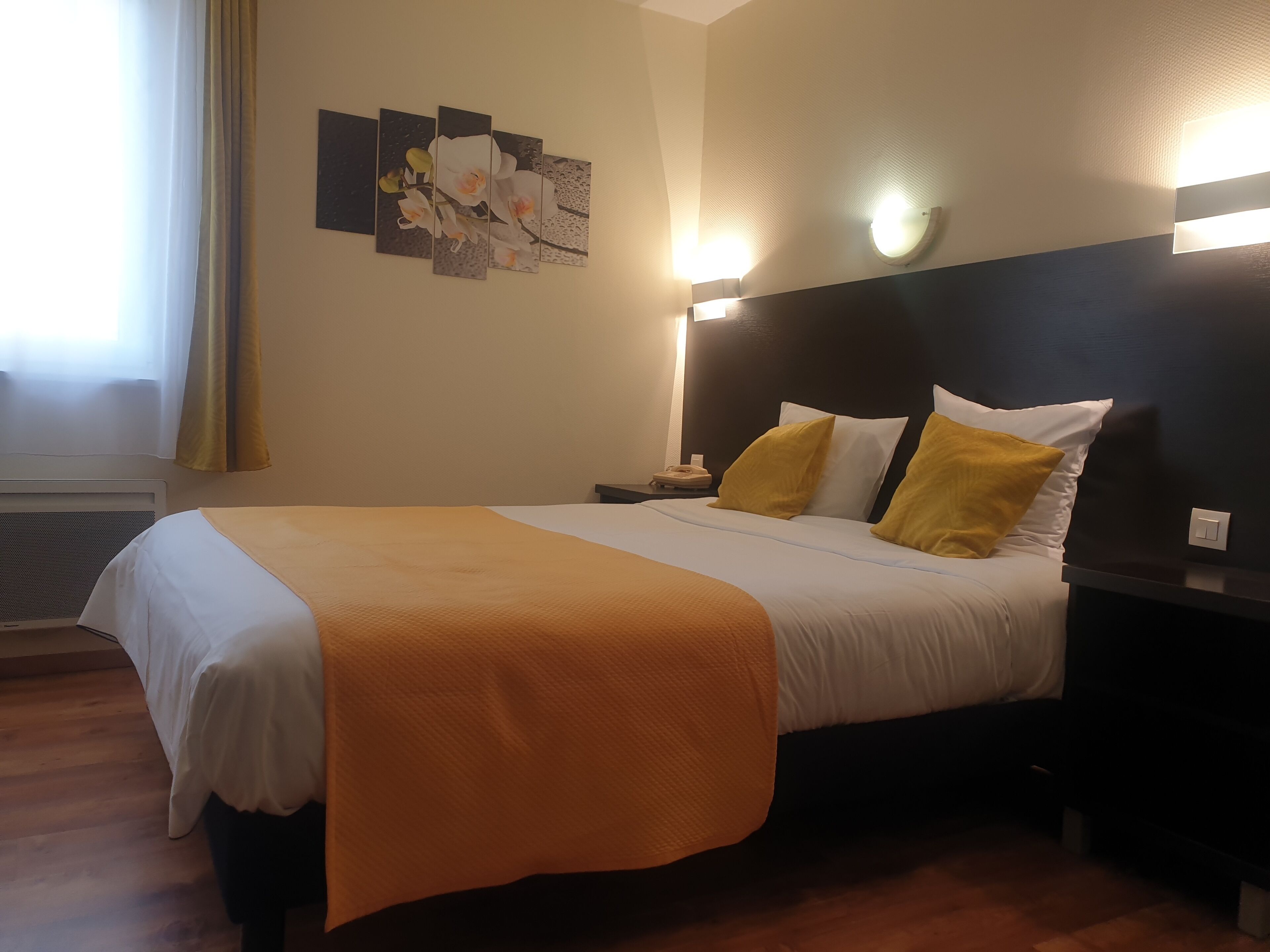 Una camera d'albergo con un letto, un comodino, una lampada a parete e una finestra con tende.