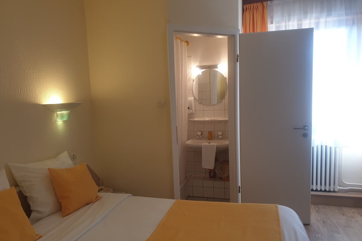 Une chambre d’hôtel avec un lit, une salle de bain visible à travers une porte ouverte et un luminaire fixé au mur.