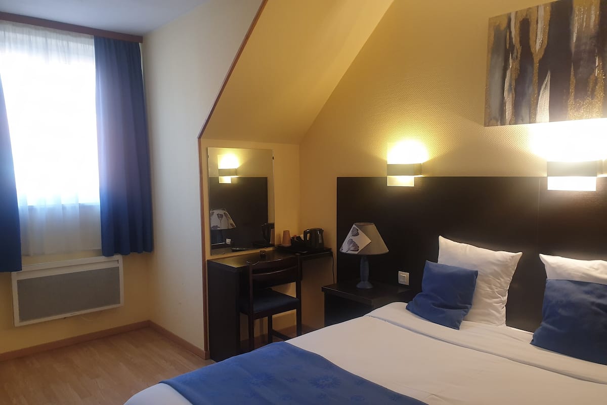 Une chambre d’hôtel avec un lit, un bureau, une chaise, une lampe et un miroir.