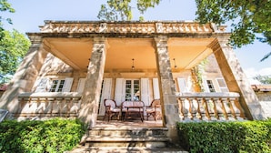 A stone building with a covered porch, columns, and a table with chairs. - Garden Oasis Pool Villa (Konavle)