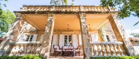 A stone building with a covered porch, columns, and a table with chairs.