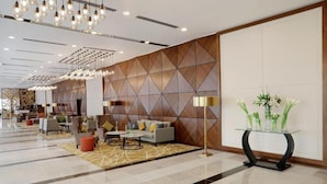 Un hall d’entrée moderne avec un mur orné d’un motif géométrique, un espace détente avec des canapés et des tables, et un vase en verre rempli de fleurs posé sur une console.
