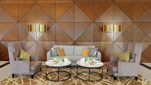 Un espace détente moderne avec un mur orné d’un motif géométrique, deux fauteuils, un canapé et des tables rondes sur lesquelles sont disposées des boissons.