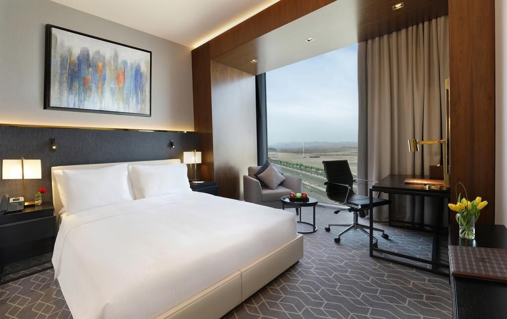 Quarto de hotel com cama grande, escrivaninha, cadeira e vista da cidade.