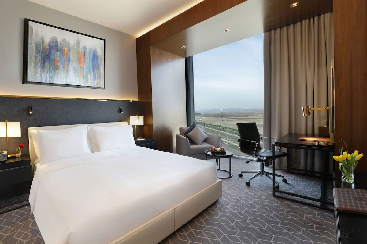 Ein modernes Hotelzimmer mit einem großen Bett, einem Schreibtisch, einem Stuhl und Blick auf die Landschaft.