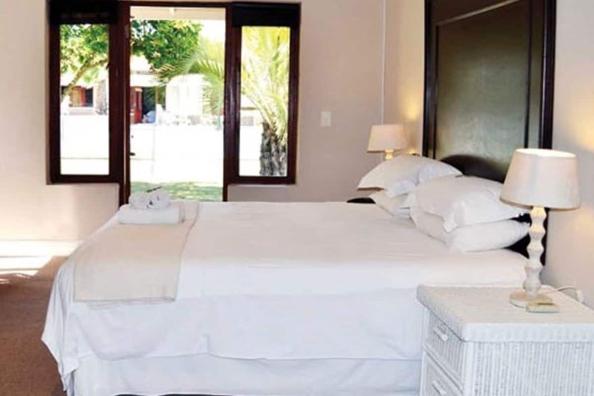 Une chambre à coucher avec un grand lit, deux tables de chevet avec des lampes, une fenêtre donnant sur un paysage verdoyant et une tête de lit sombre.