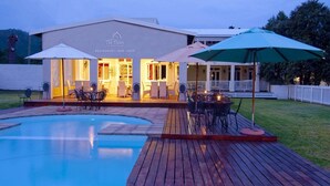 Un espace aménagé au bord de la piscine, avec une terrasse en bois, des sièges d’extérieur et des parasols.