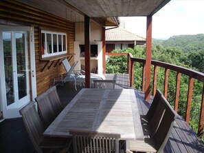 Une terrasse en bois avec une table et des chaises, donnant sur un paysage boisé.