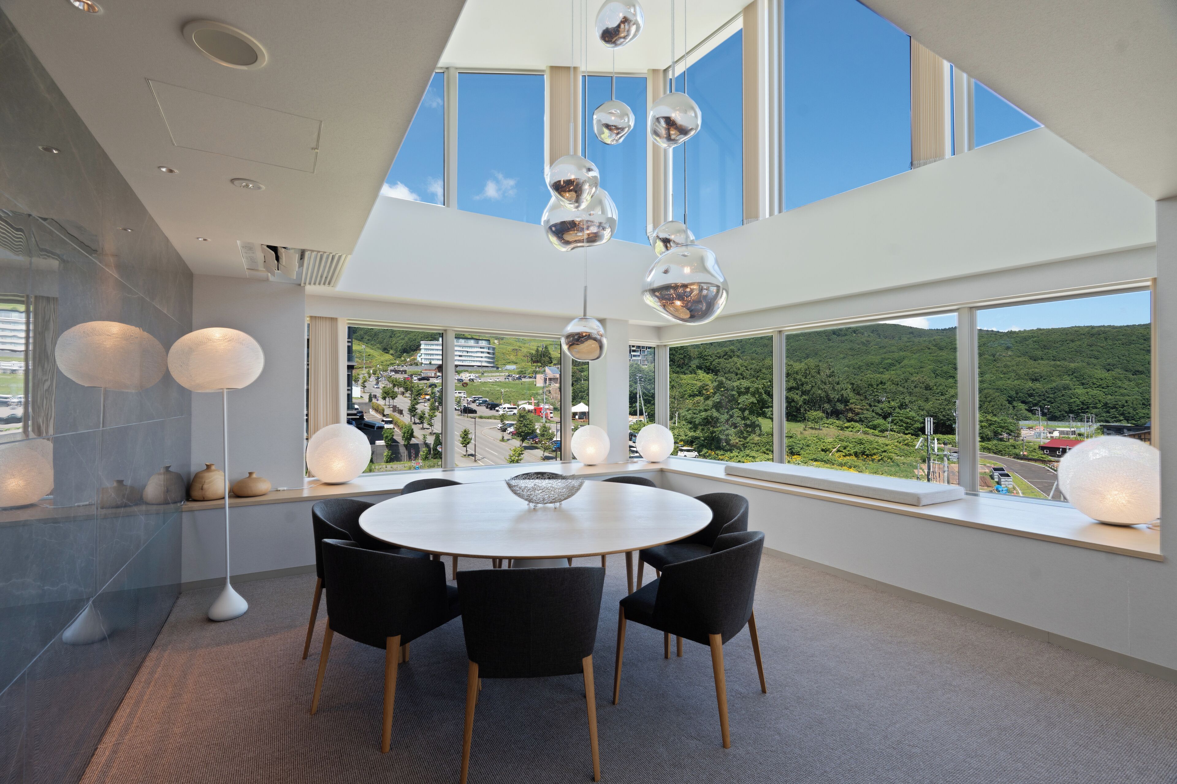 A modern dining area with a round table, black chairs, and hanging spherical light fixtures.
