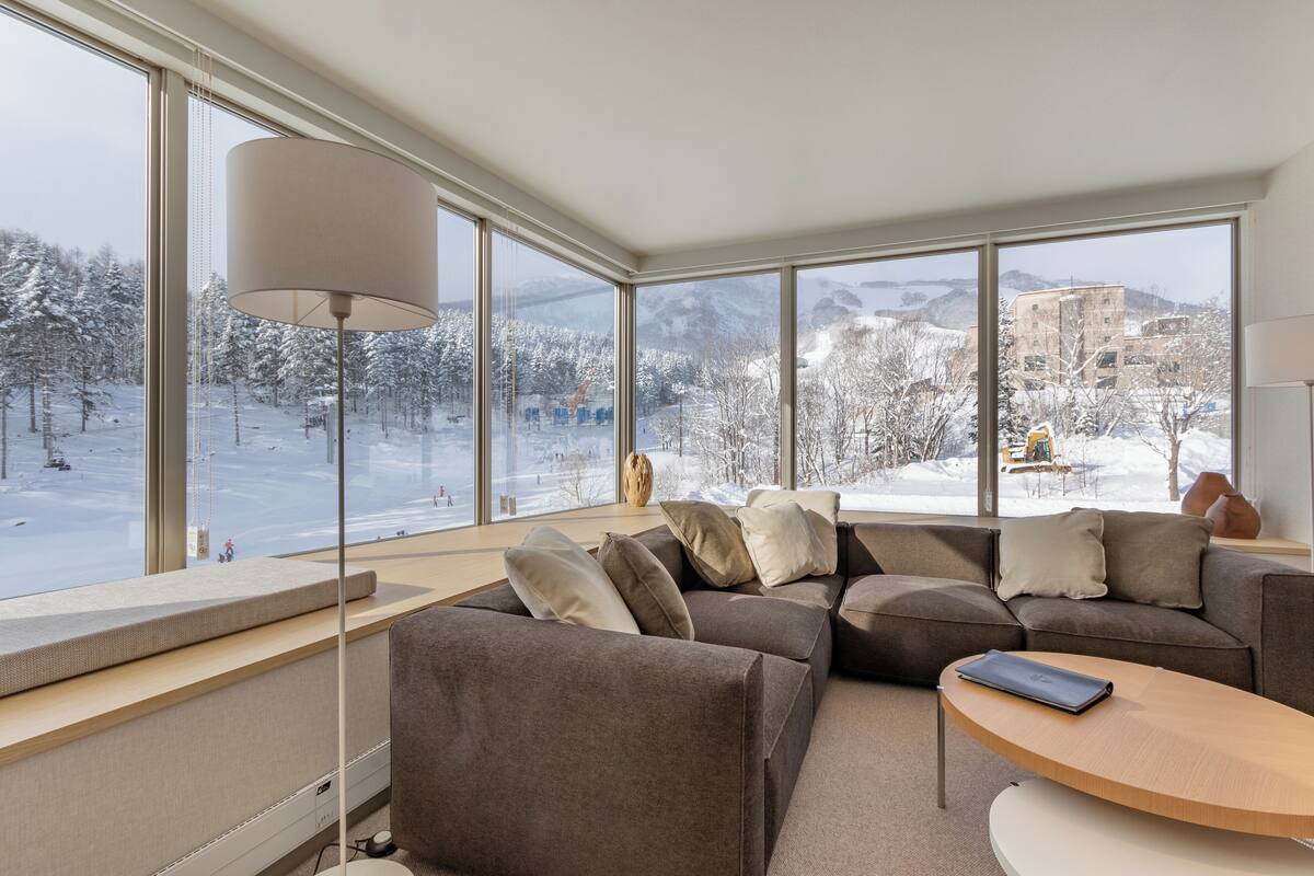 A modern living room with a large window, a sofa, a lamp, and a laptop on a table.