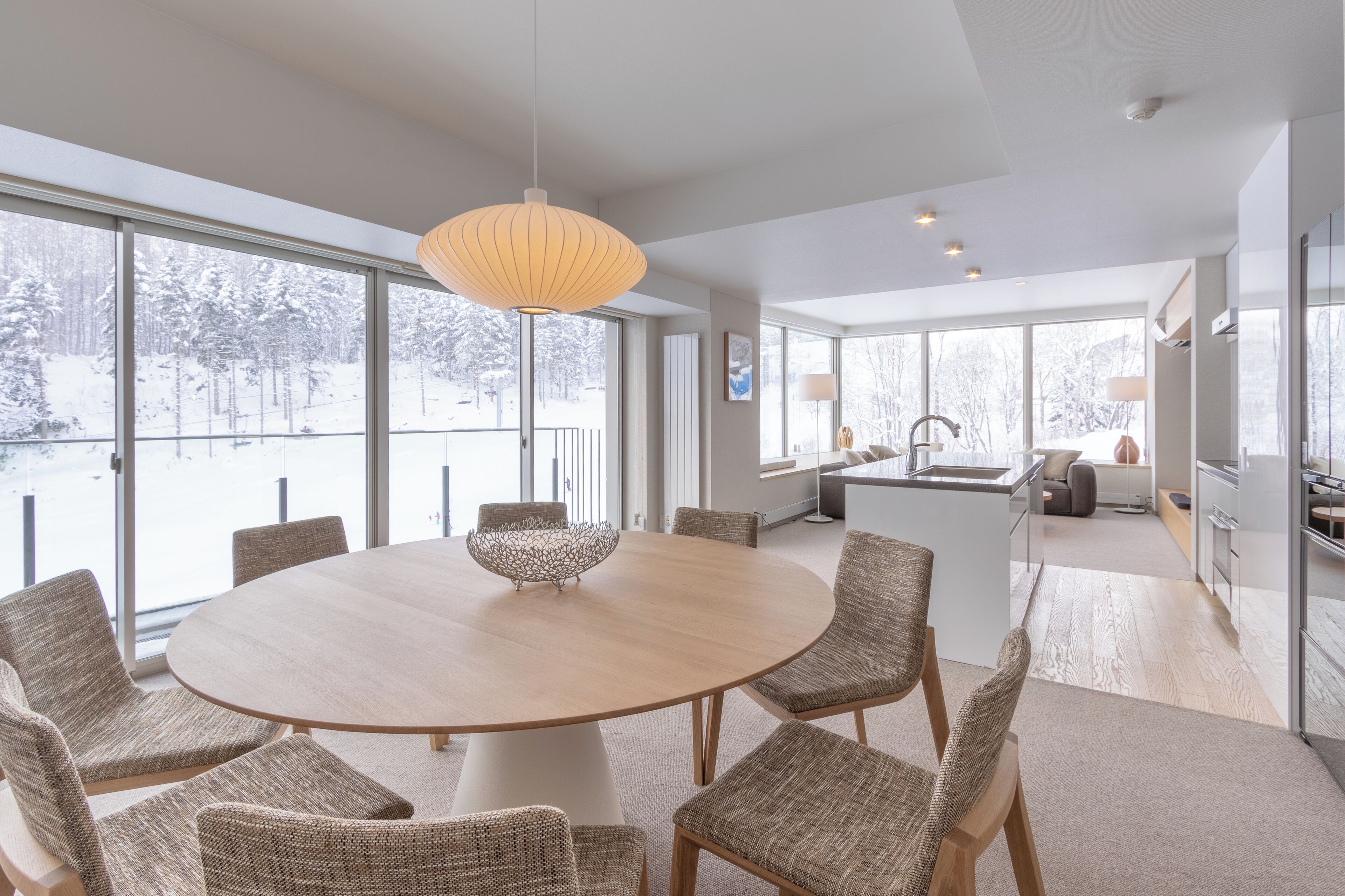 A modern dining area with a round table, wicker chairs, and a hanging light fixture.
