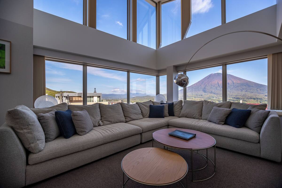 A modern living room with a large sectional sofa, a round coffee table, and large windows offering a view of a mountain.