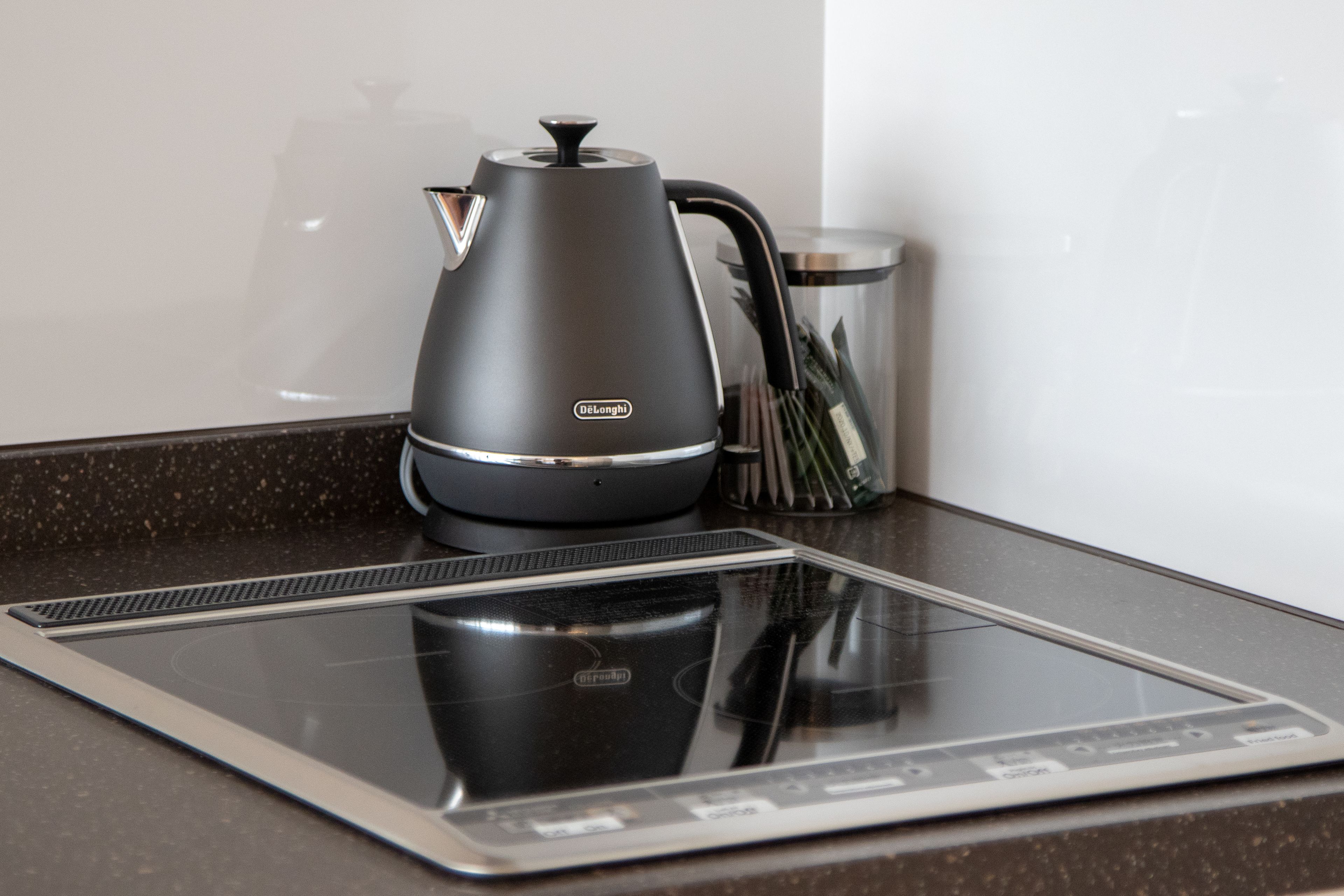 A modern kitchen with a sleek induction cooktop, a black electric kettle, and a stainless steel trash can.