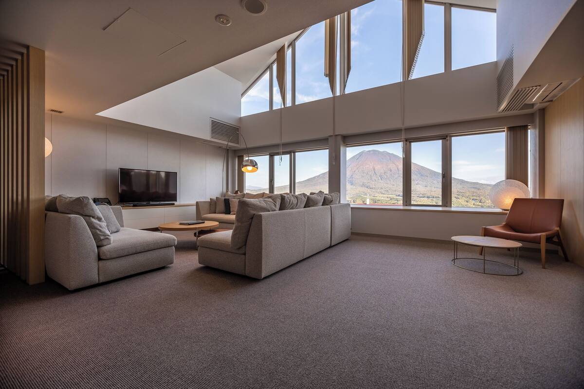 A modern living room with a large sectional sofa, a small round table, and a TV mounted on the wall.