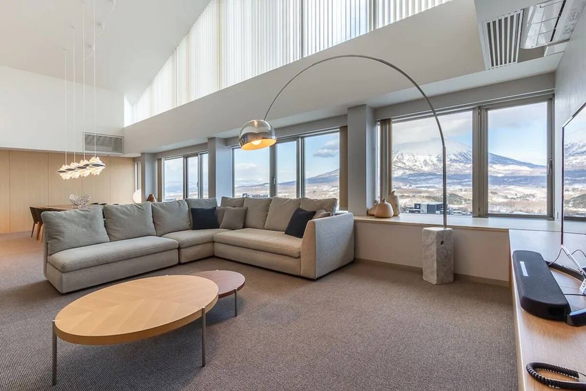A modern living room with a large sectional sofa, a round coffee table, and a view of a mountainous landscape through large windows.
