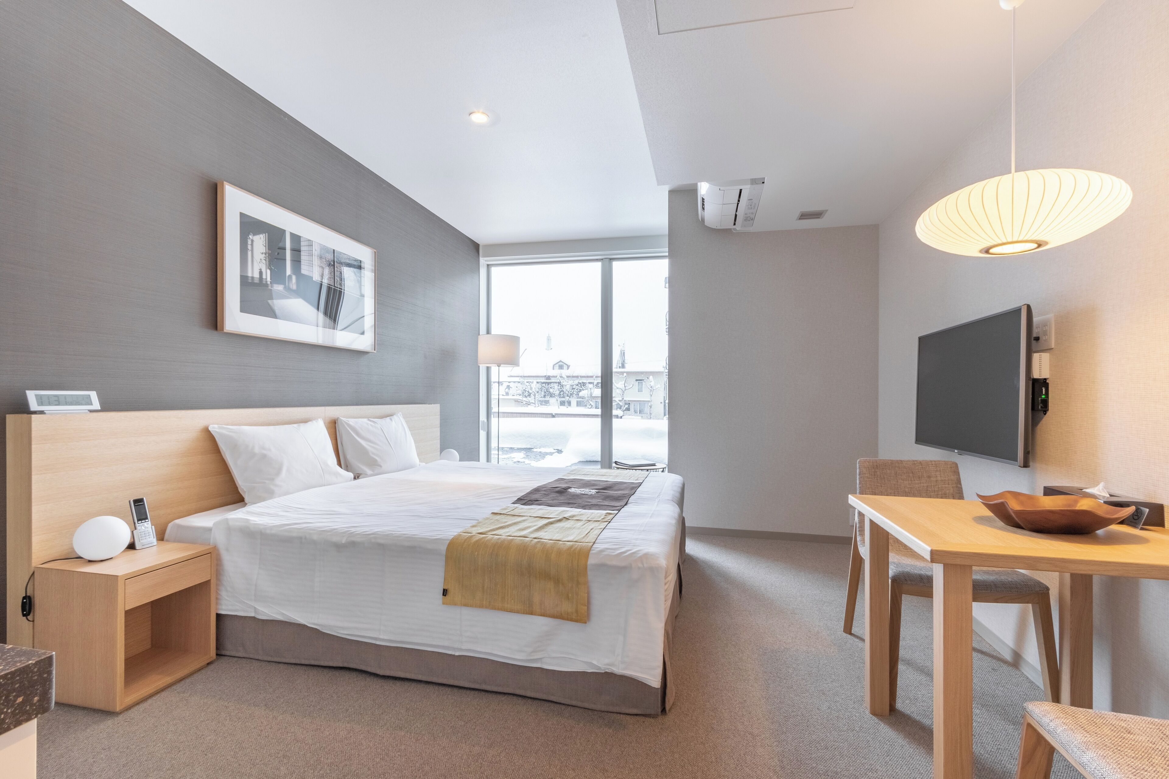Una habitación de hotel moderna con una cama grande, un escritorio, una silla, un televisor y una ventana con vistas.