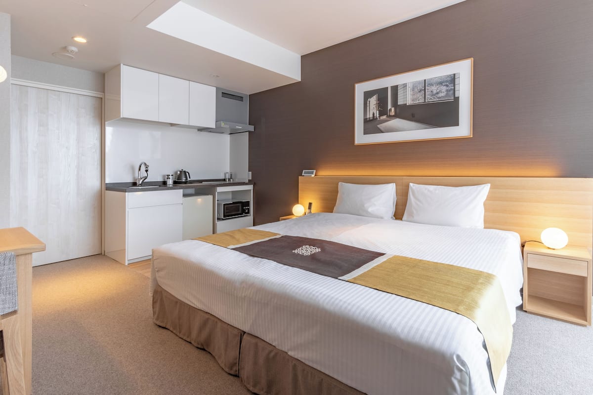 A modern hotel room with a large bed, a kitchenette, and a view of the city.