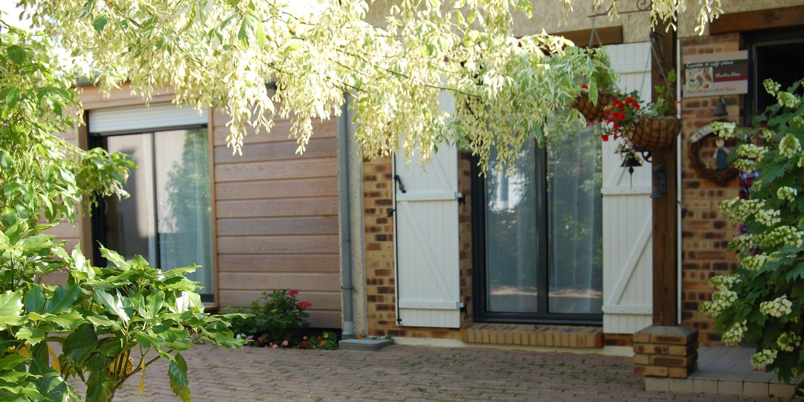 Ein Backsteinhaus mit großer Schiebetür, einer kleinen Veranda mit Topfpflanzen und hängenden Blumenkörben.
