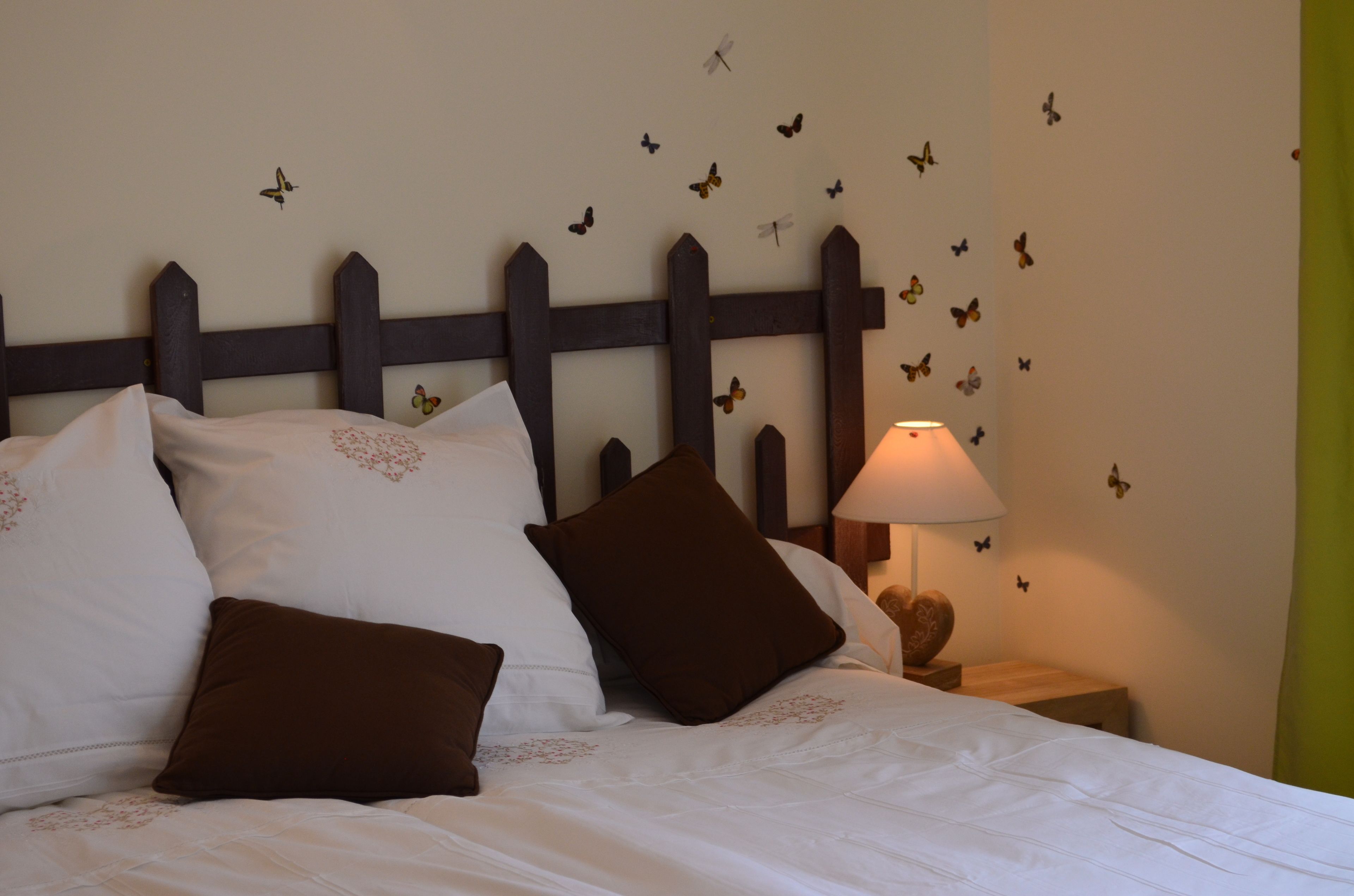 Una cama bien hecha con ropa de cama blanca y marrón, un cabecero de madera y una pared decorada con adhesivos de mariposas.