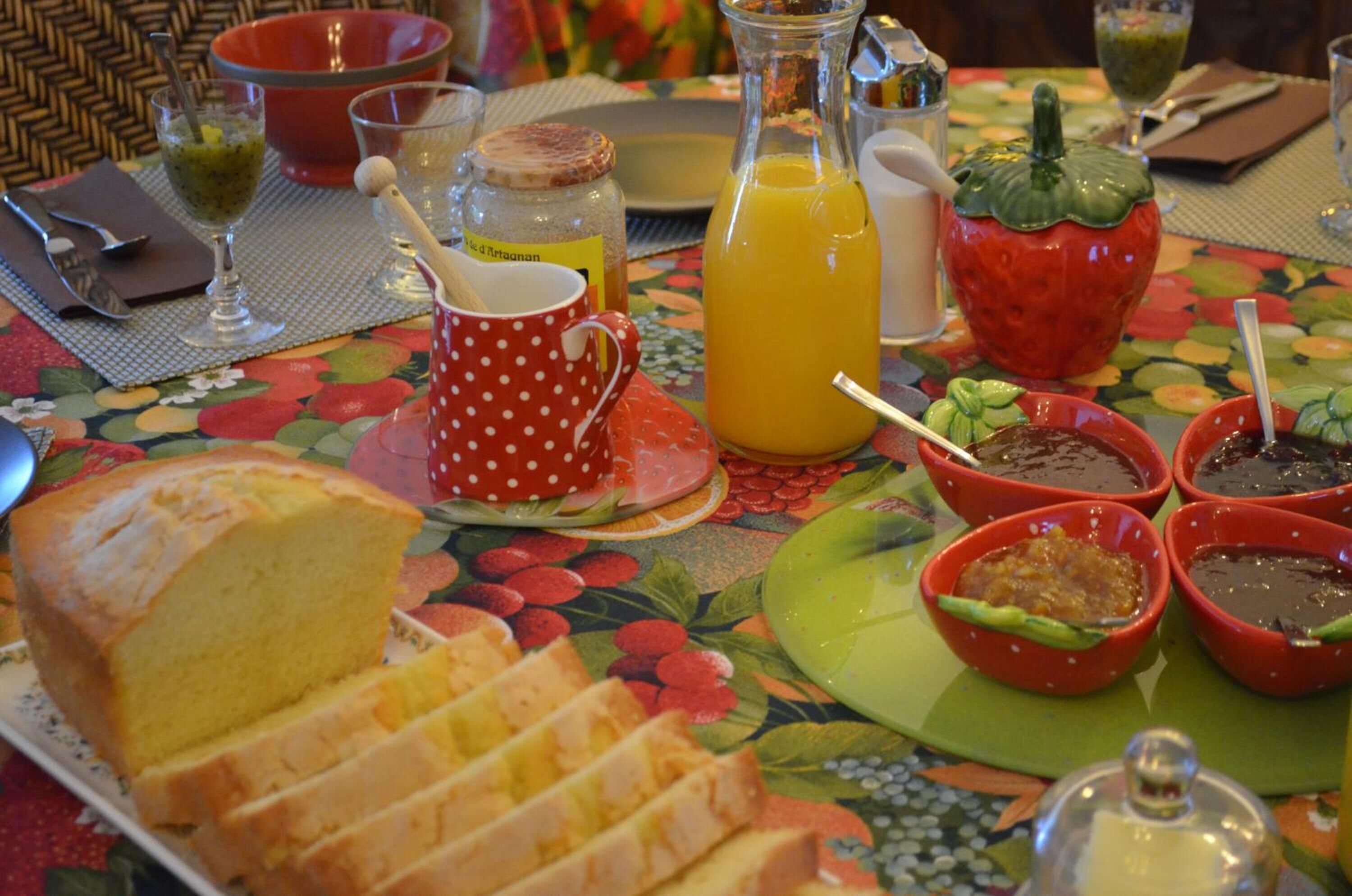 Een ontbijttafel met een brood, een mok met stippen, een fles sinaasappelsap en verschillende kleine schaaltjes met toevoegingen.