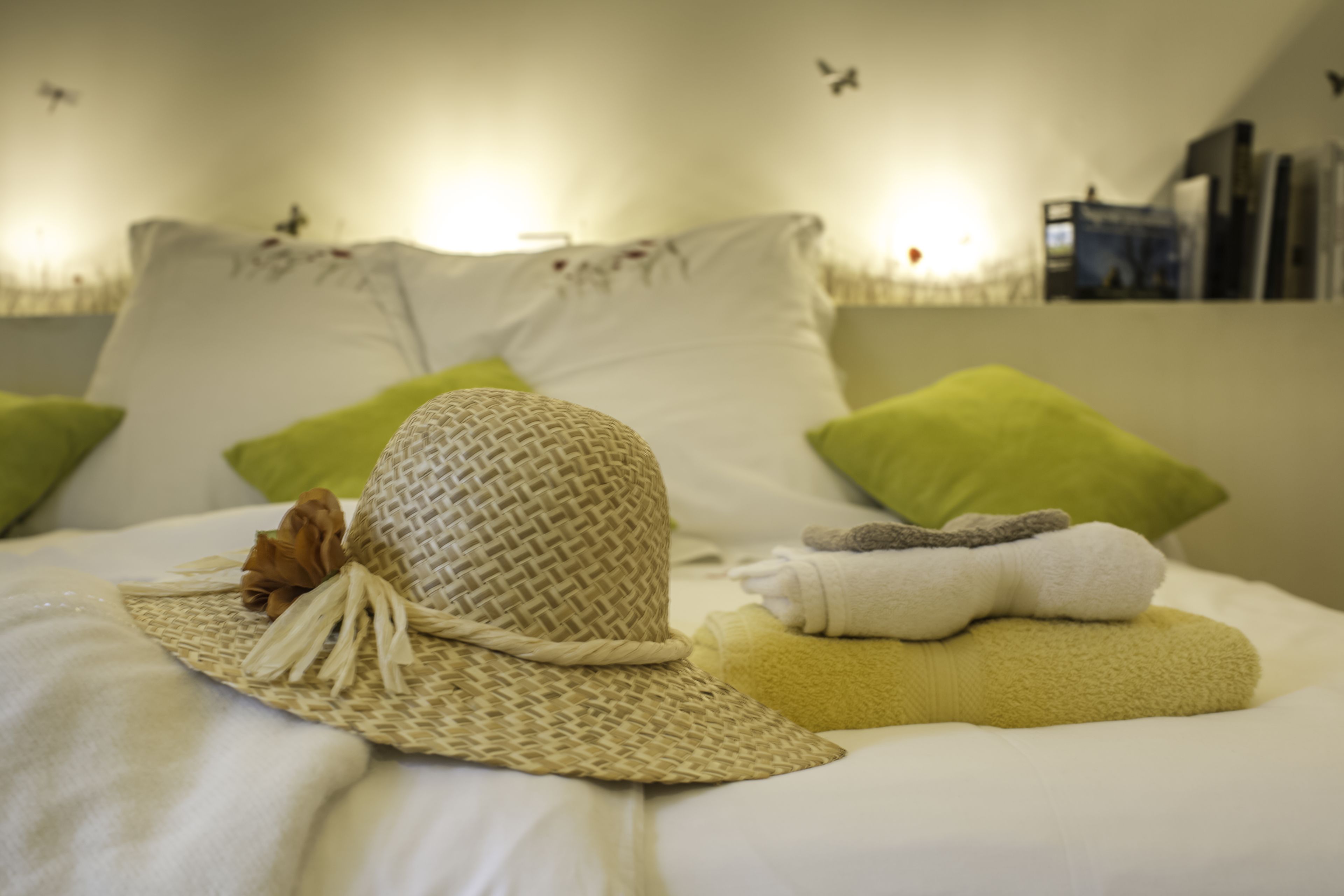 A neatly made bed with a woven hat, green pillows, and folded towels.