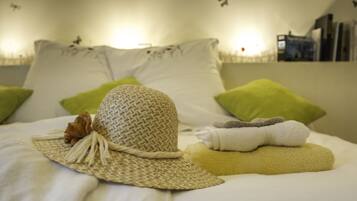 A neatly made bed with a woven hat, green pillows, and folded towels.