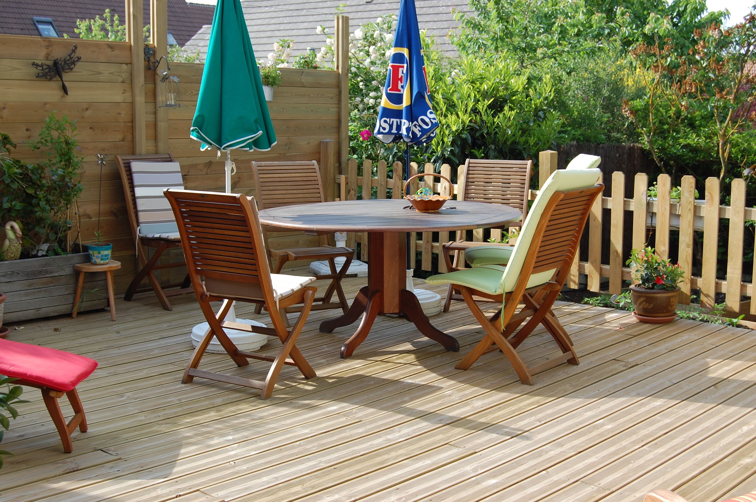 A wooden deck with a round table and four chairs, surrounded by a wooden fence and potted plants.
