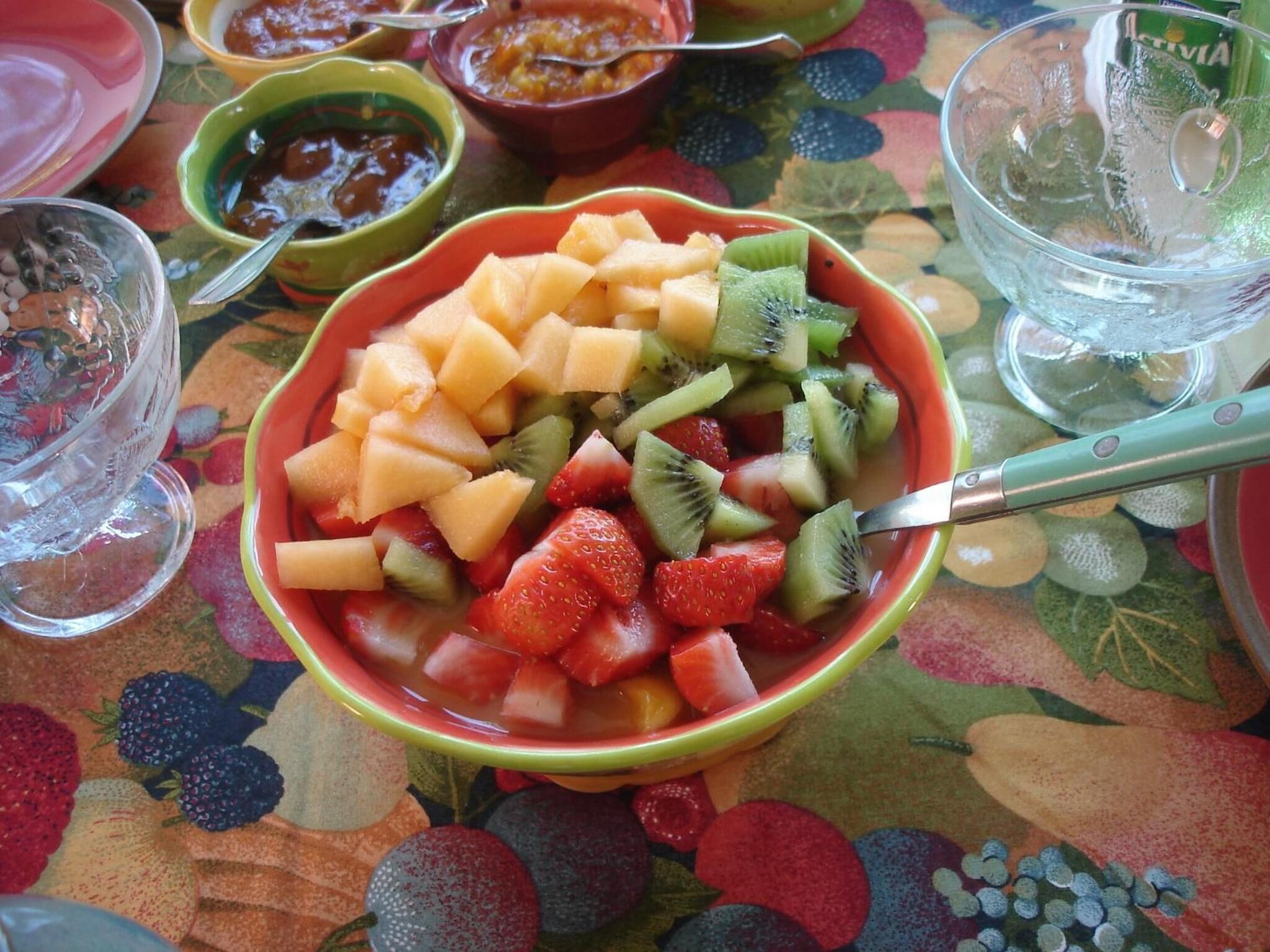 Eine Schüssel gemischten Obstsalats auf einem Tisch mit farbenfroher Tischdecke.